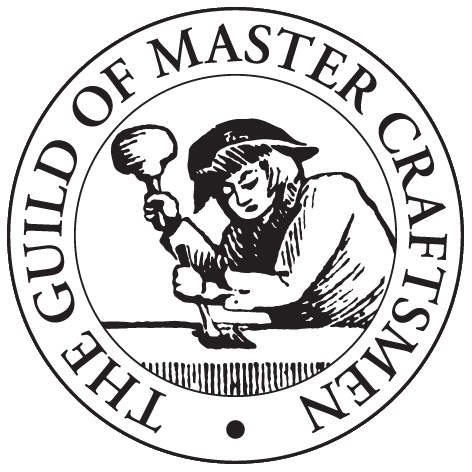 Black and white logo of The Guild of Master Craftsmen, featuring an illustrated craftsman hammering a chisel on a surface, surrounded by the organization's name in a circular border.