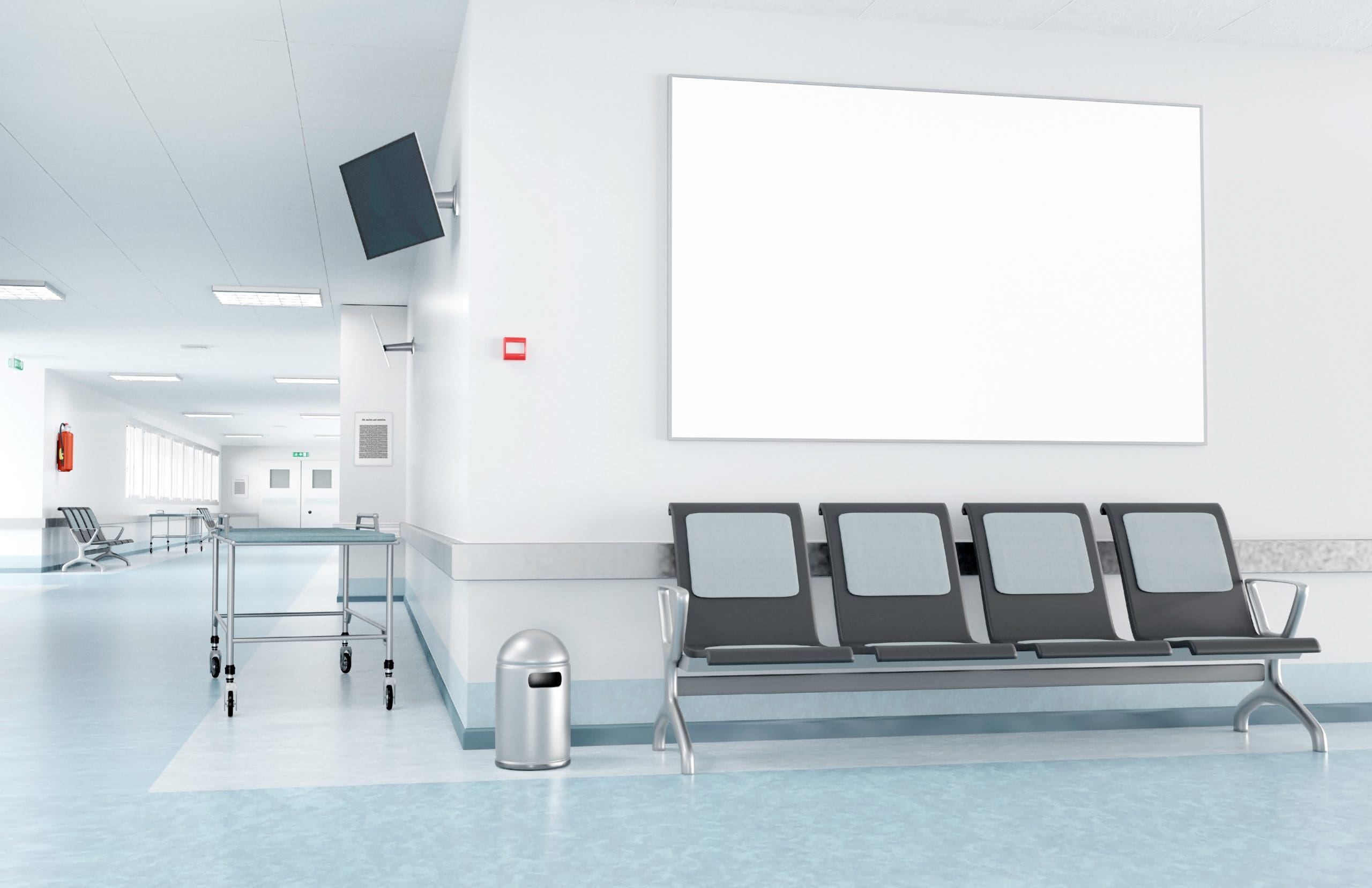 A modern hospital corridor with light blue flooring, gray-blue walls, and bright lighting. There's a row of four gray chairs, an empty stretcher trolley, a small trash can, a wall-mounted TV, and a large blank white board on the wall.