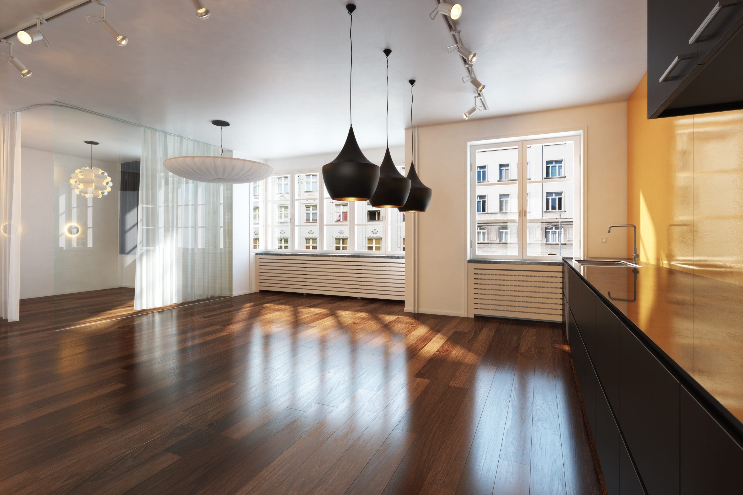 A spacious, modern kitchen with dark wooden floors and ceiling spotlights. It features sleek black cabinets, pendant lights, and large windows with a view of neighboring buildings. A glass partition separates a bright, open dining area.