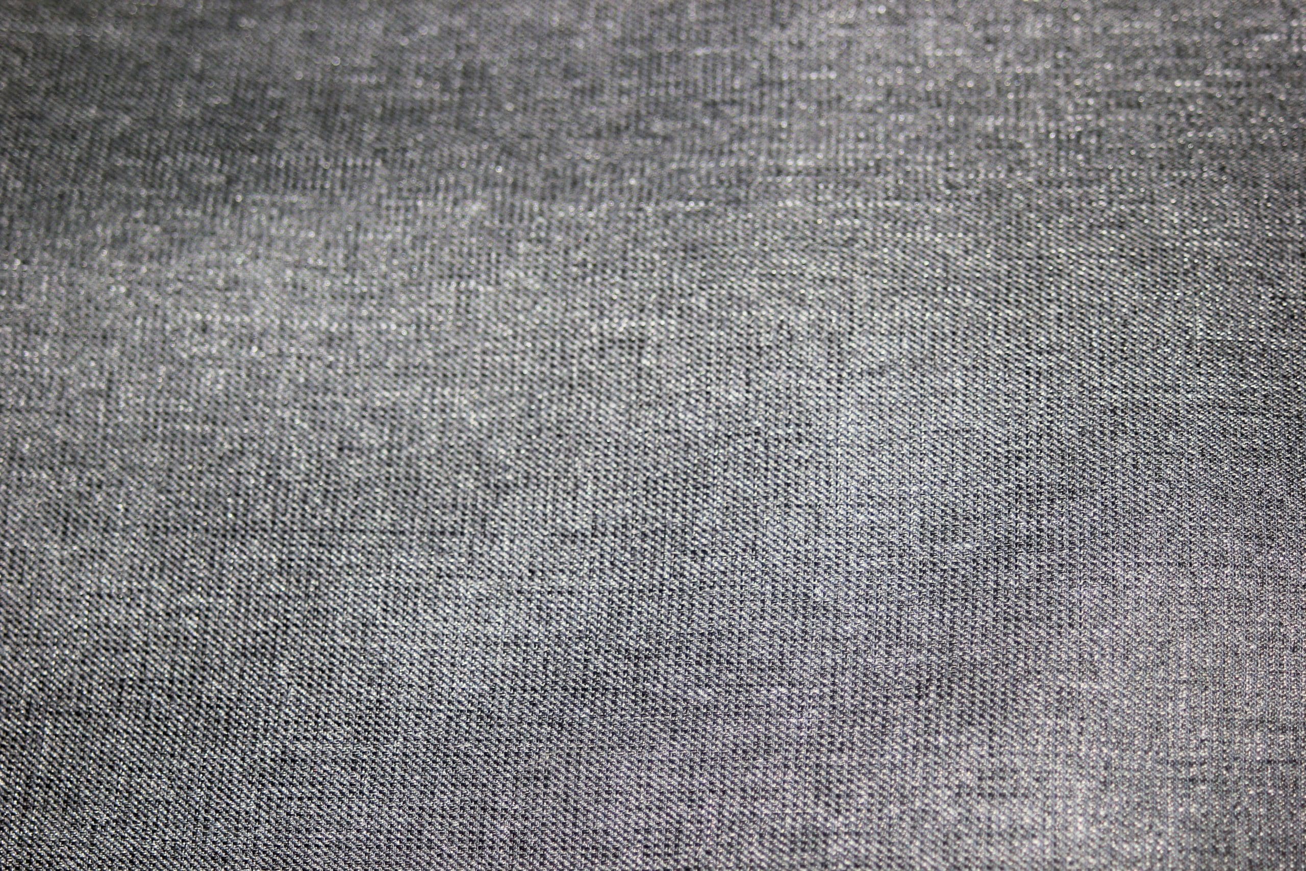 Close-up of a smooth, textured surface of gray fabric, showing its woven pattern and subtle variations in shade. The textile appears soft and slightly reflective under the light.