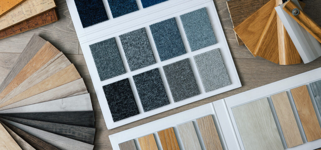 Assorted flooring and carpet swatches arranged on a table, including samples of blue and gray carpets and various shades of wood and laminate flooring.